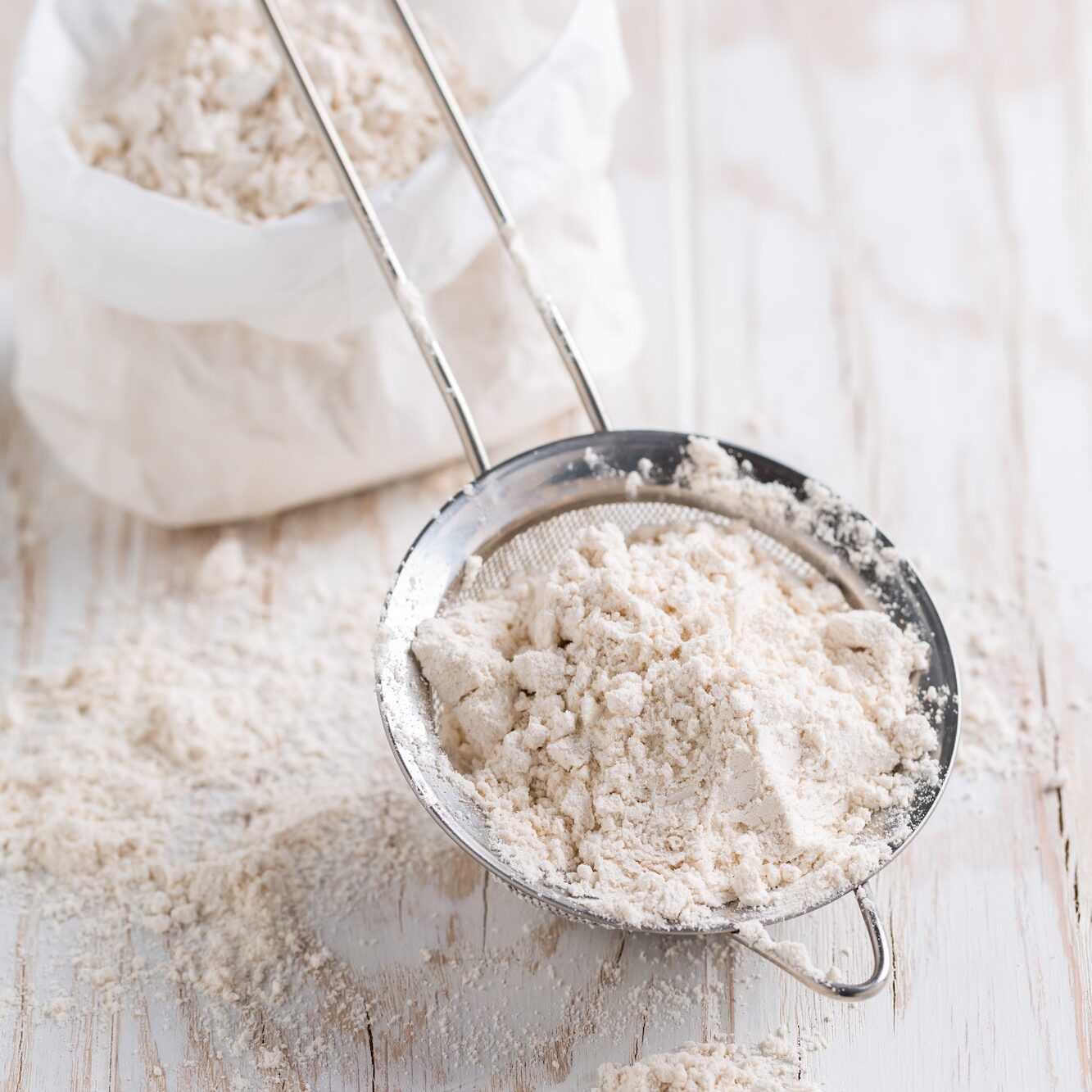 Spelt flour in sifter in flour bag on white wooden table